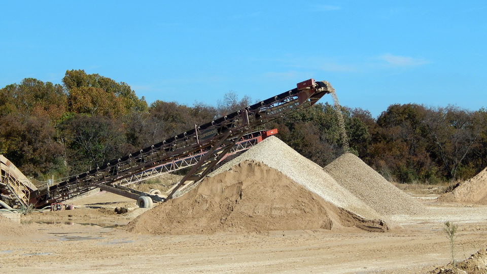 A large pile of sand is being loaded into a conveyor belt.